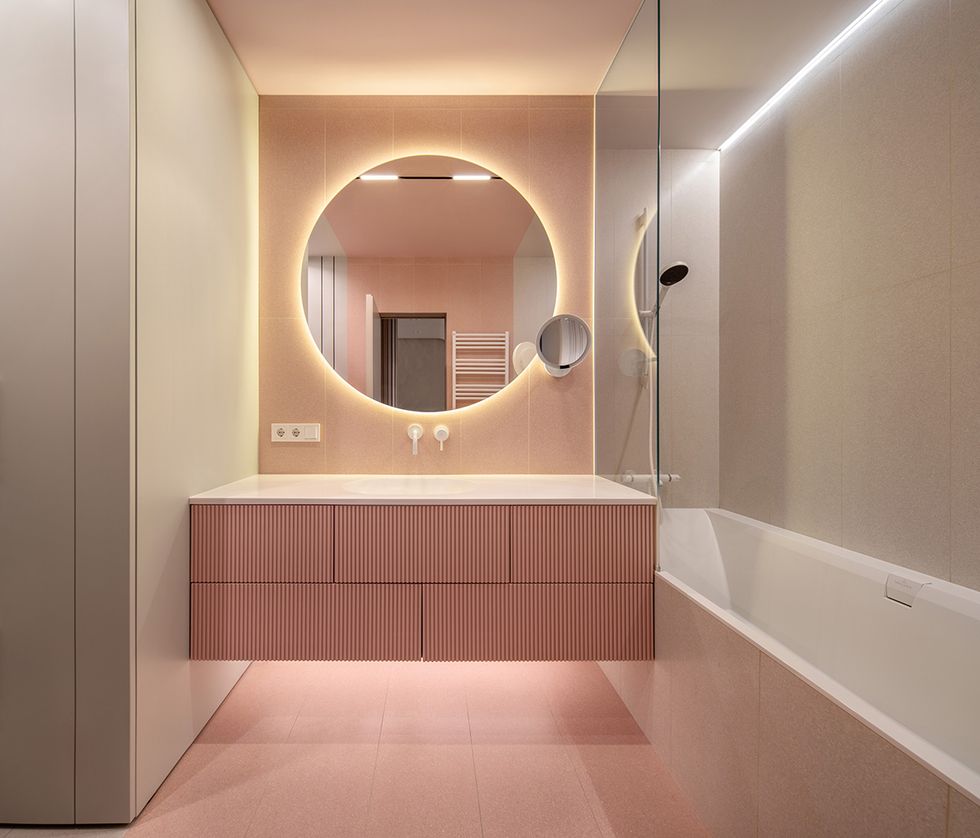un aseo con muebles, banera y suelos, todo en color rosa, y un espejo retroiluminado