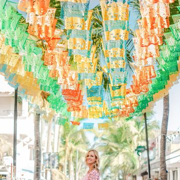 summer thornton standing under the flags in sayulita mexico with a guide to shops and restaurants