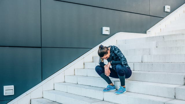 jonge, vermoeide vrouwelijke hardloper zit op trap in sportkleding