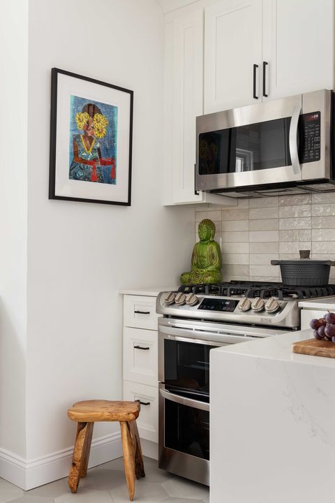 white cabinets, wooden stepping stool, oven, stainless steel microwave, wall art, green buddha statue