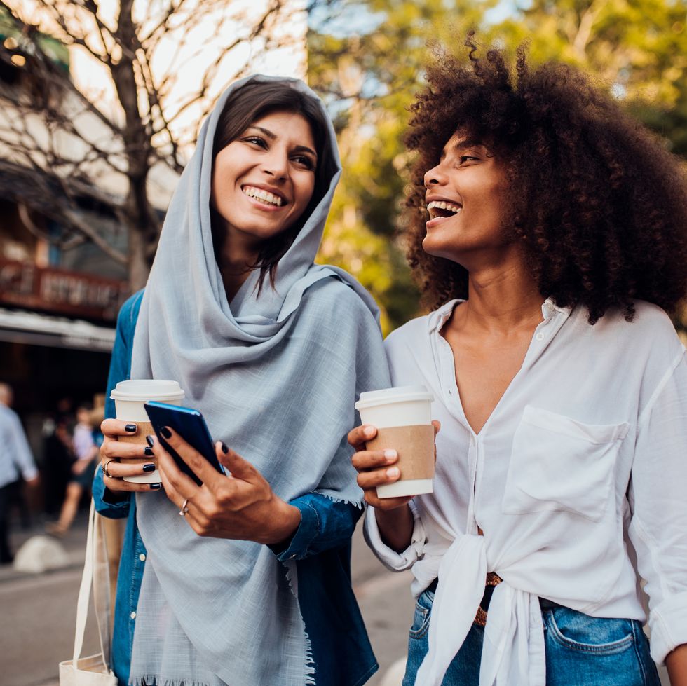 portrait of two young women drinking coffee whilst walking in the streets
