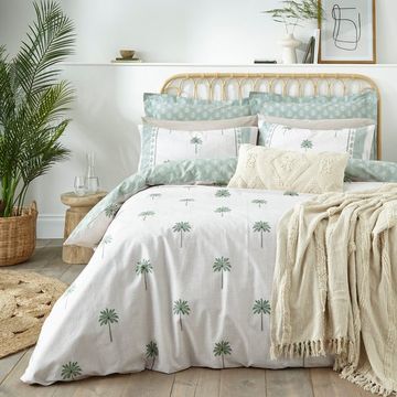bed with palm tree print bedding, a table and large plant