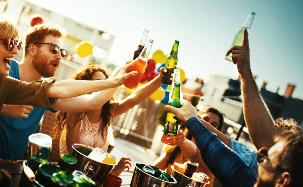 closeup shot of a group of young adults seated at a big table on a rooftop terrace, having some light drinks, talking and laughing