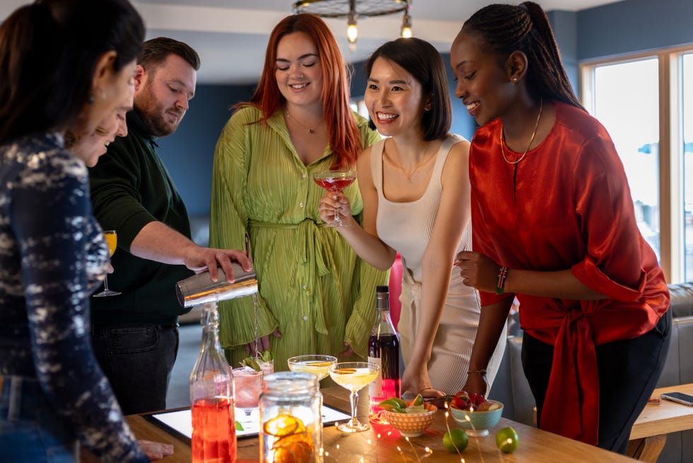 group of colleagues participating in a cocktail making class as a bartender pours a drink in front of them