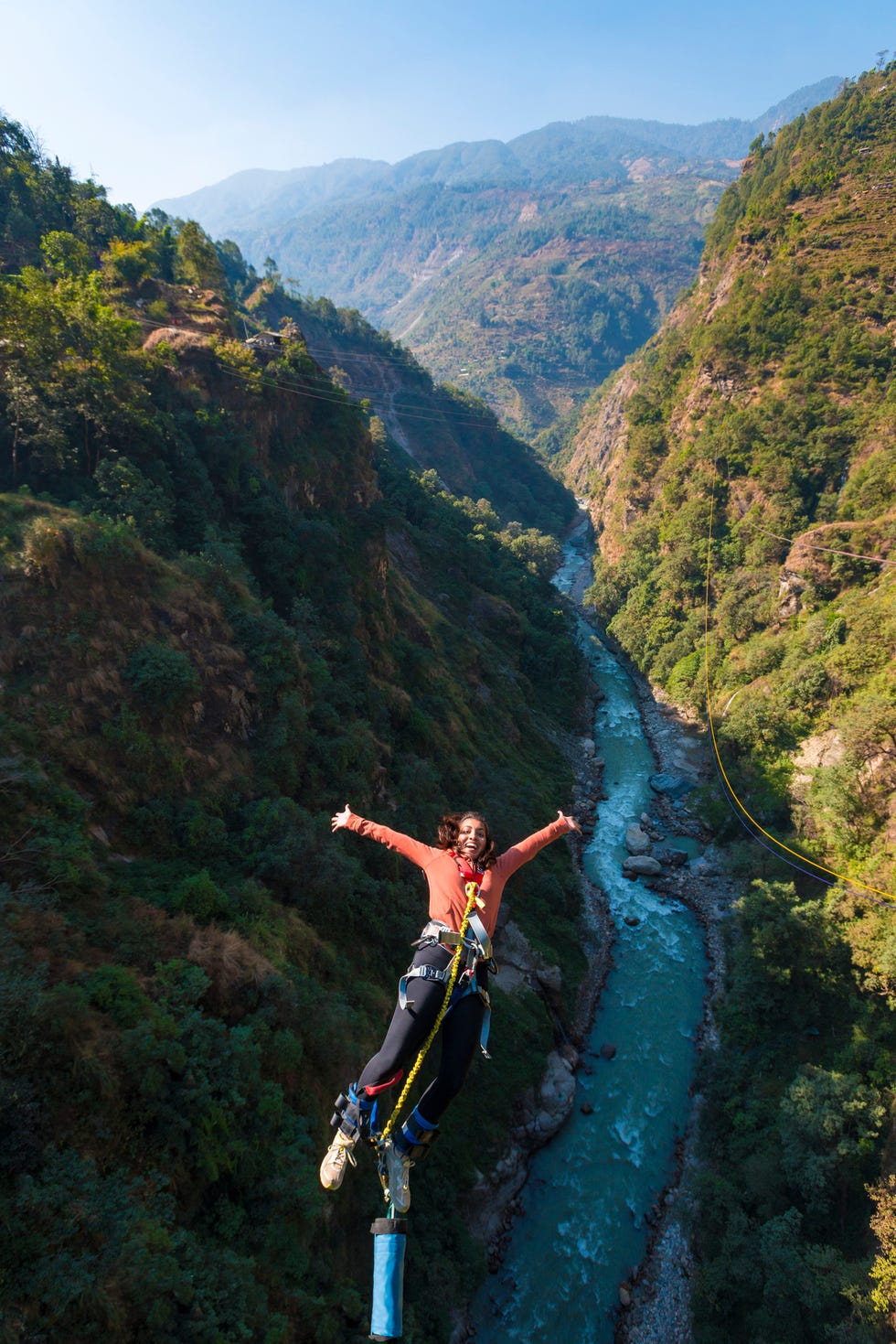 a girl bungee jumps from a bridge spanning a gorge in nepal