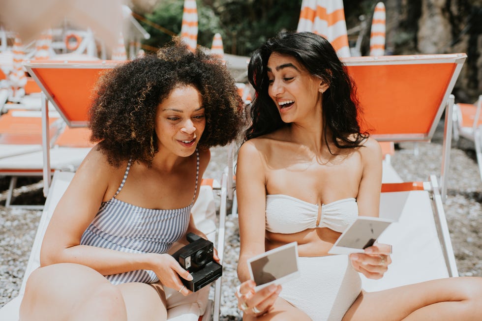 two woman compare instant photo prints taken on a camera whilst on holiday