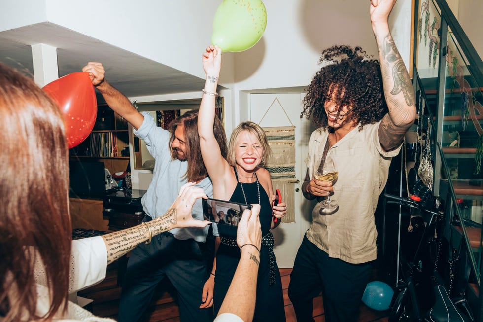 woman taking a picture of a bunch of friends dancing during a house party and drinking