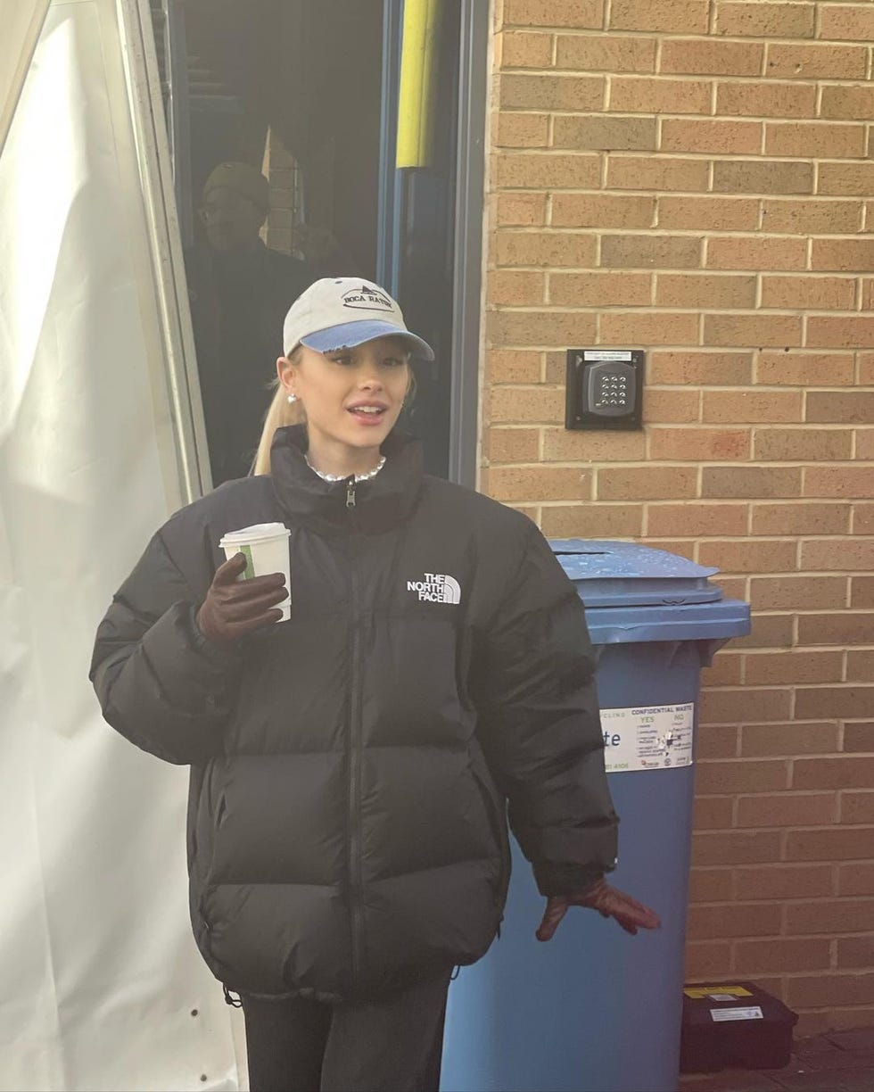 person wearing a black puffer jacket holding a coffee cup outside a building