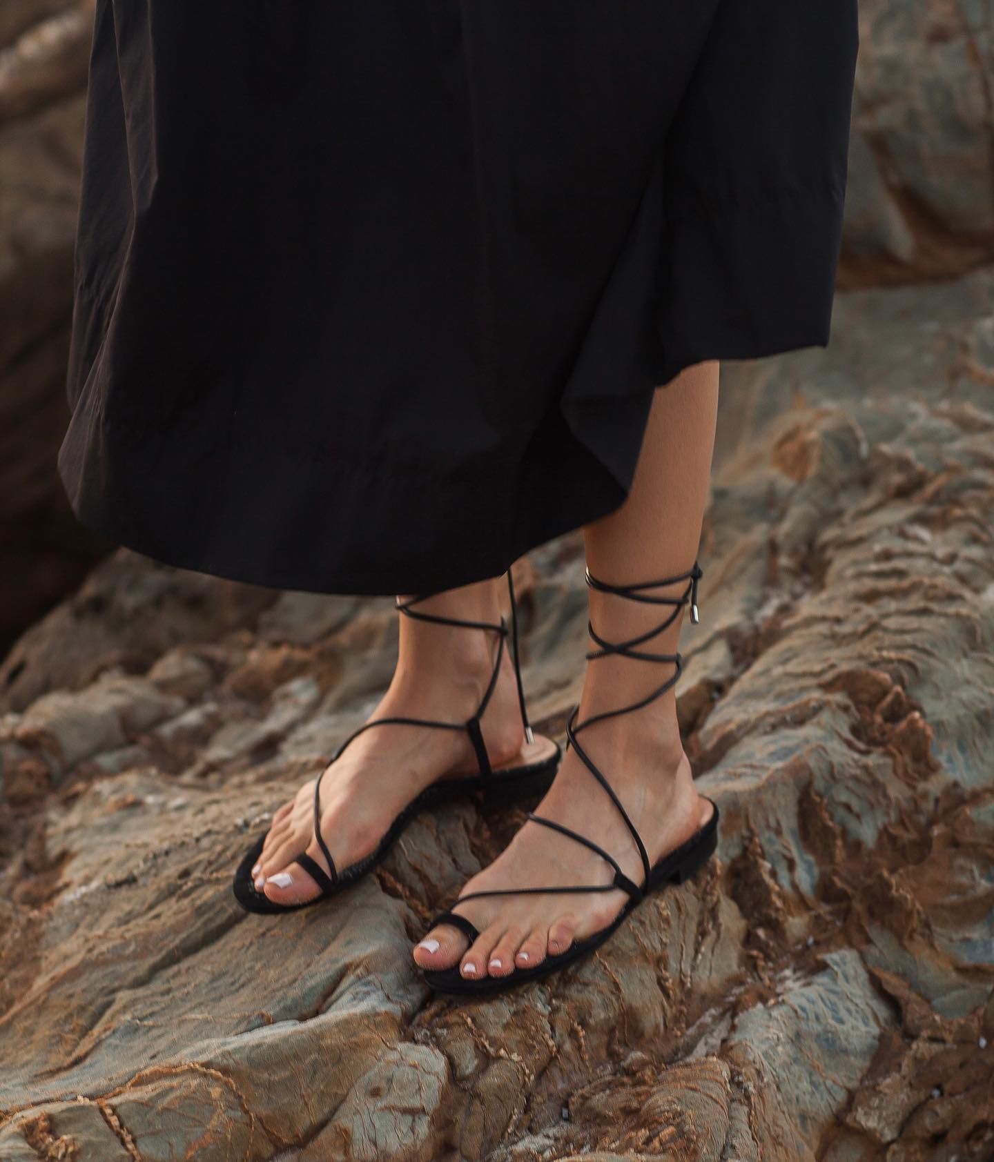 a girl in strappy sandals standing on a coastal rock by the beach