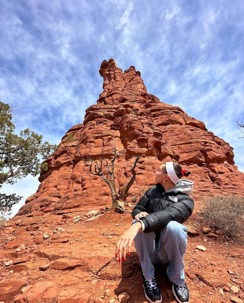 individual seated on red rocky terrain with a prominent rock formation in the background