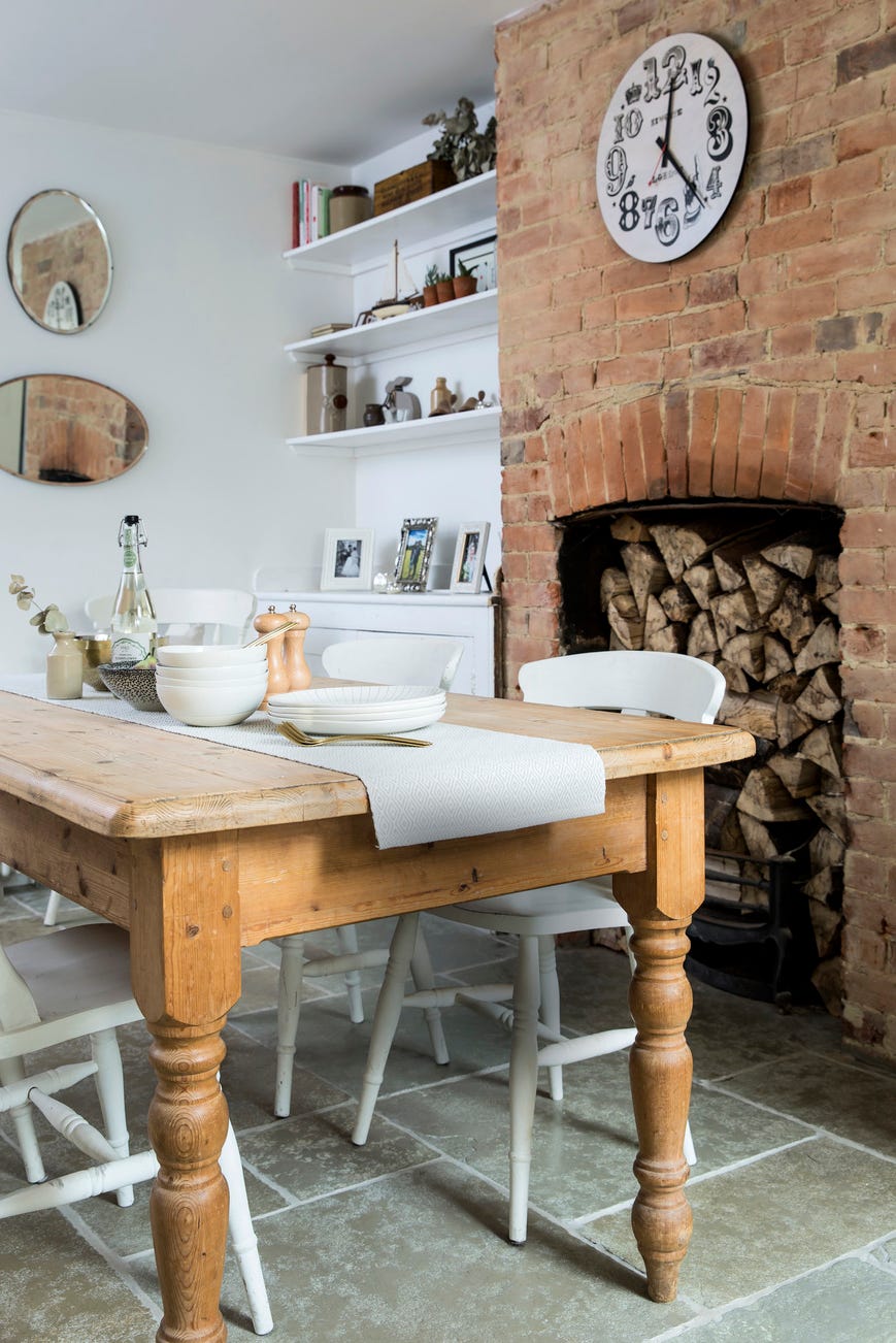 wooden dining tabel by a brick fireplace white clock hanging on the fireplace dining table the secondhand piece came complete with the characterful marks of wear and tear white chairs provide contrast and keep the look light and bright