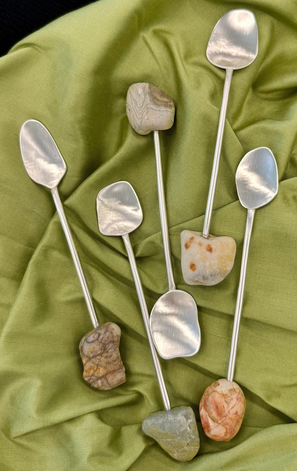 Spoons with stone handles arranged on a green fabric.