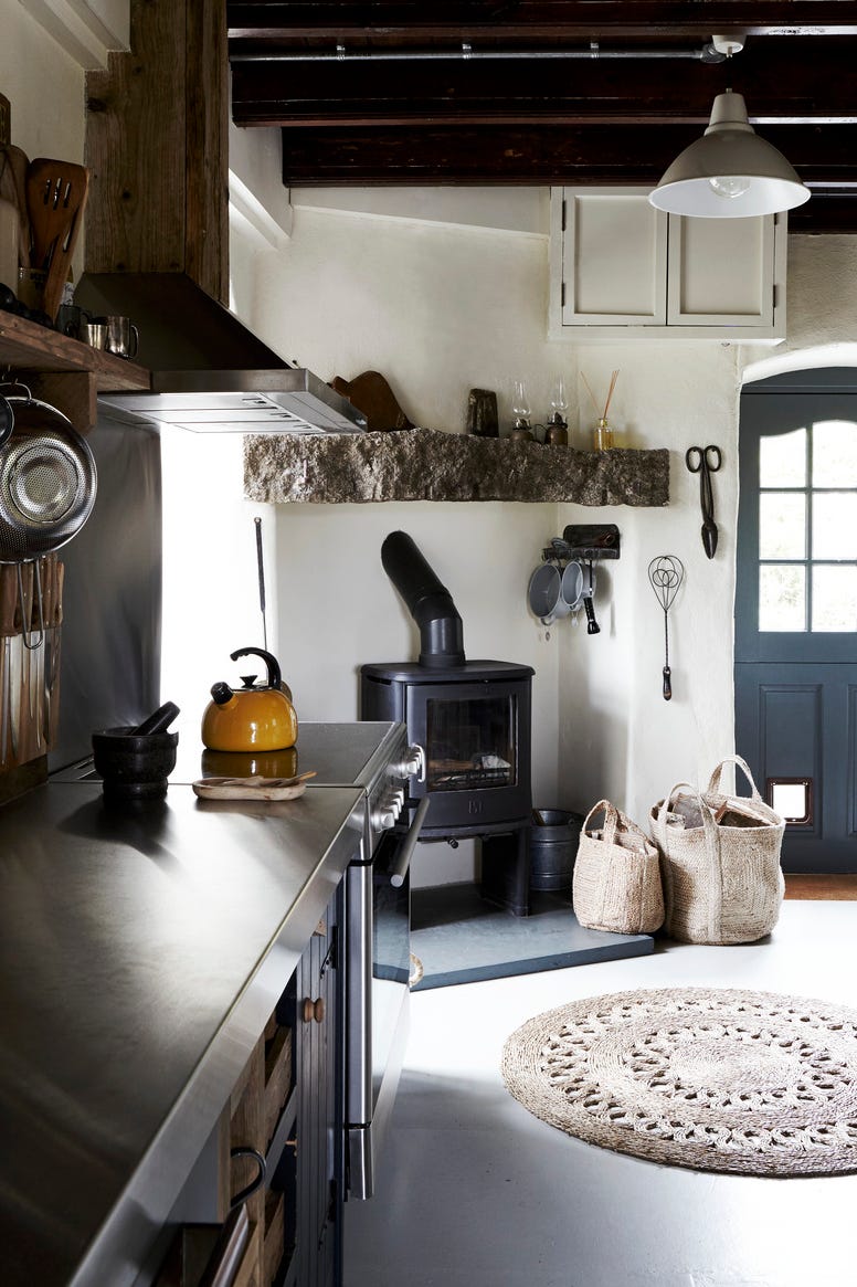 a wood burning fireplace, a blue door, yellow kettle, wooden shelves and kitchen utensils utensils double as decorative and textural elements in the kitchen of the stack, which was formerly a mine engine house the units were custom made by a carpenter and painted in farrow balls down pipe layers of local granite, plaster and timber show the make up of the building