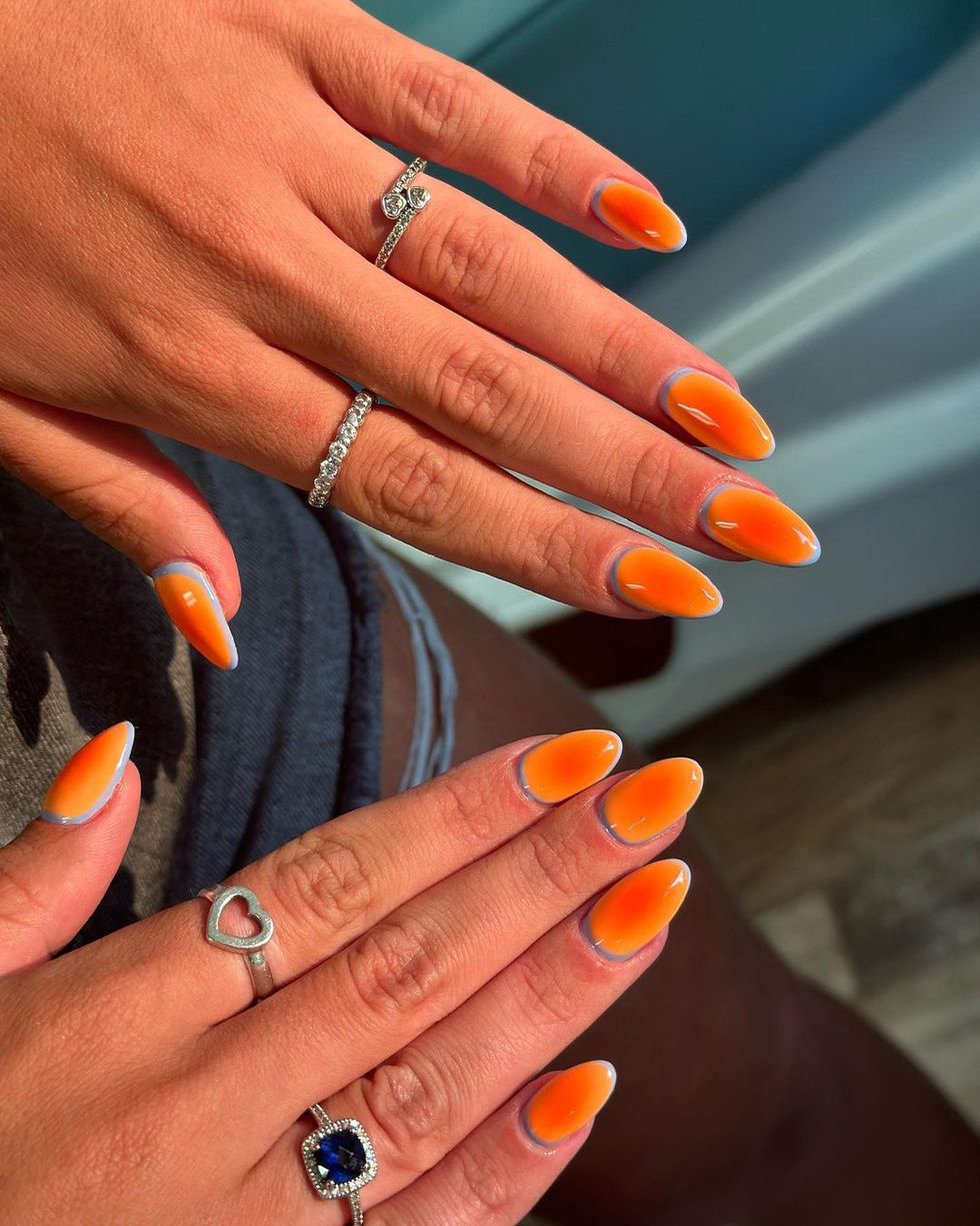 a person's hands with orange and white nails