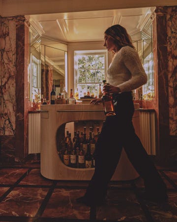 Bar counter with various bottles and a woman holding a bottle while walking beside it