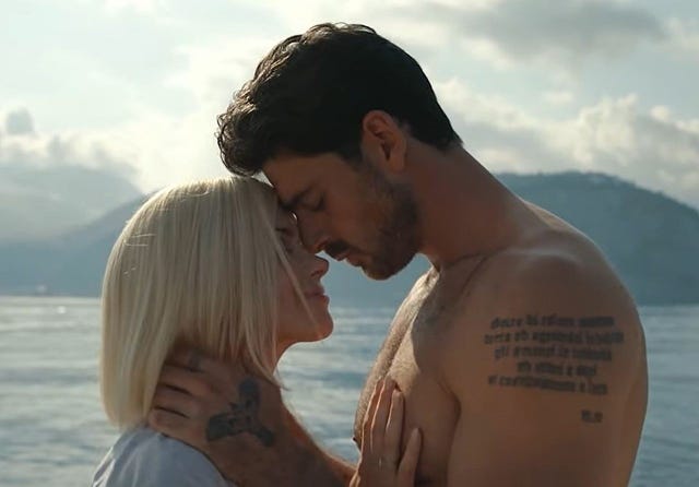 una pareja se besa en un paisaje de mar y montaña