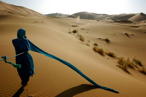 Ik nam deze foto toen ik een trektocht door de Sahara maakte Merzouga Marokko Toen ik op mijn dromedaris de omringende zandduinen aan het bewonderen was draaide ik me net op tijd om voor een blik op onze gids die zijn tulband omwikkelt Een perfecte timing en een magnifieke zonsondergang zorgden voor een van mijn favoriete fotos van de hele reis