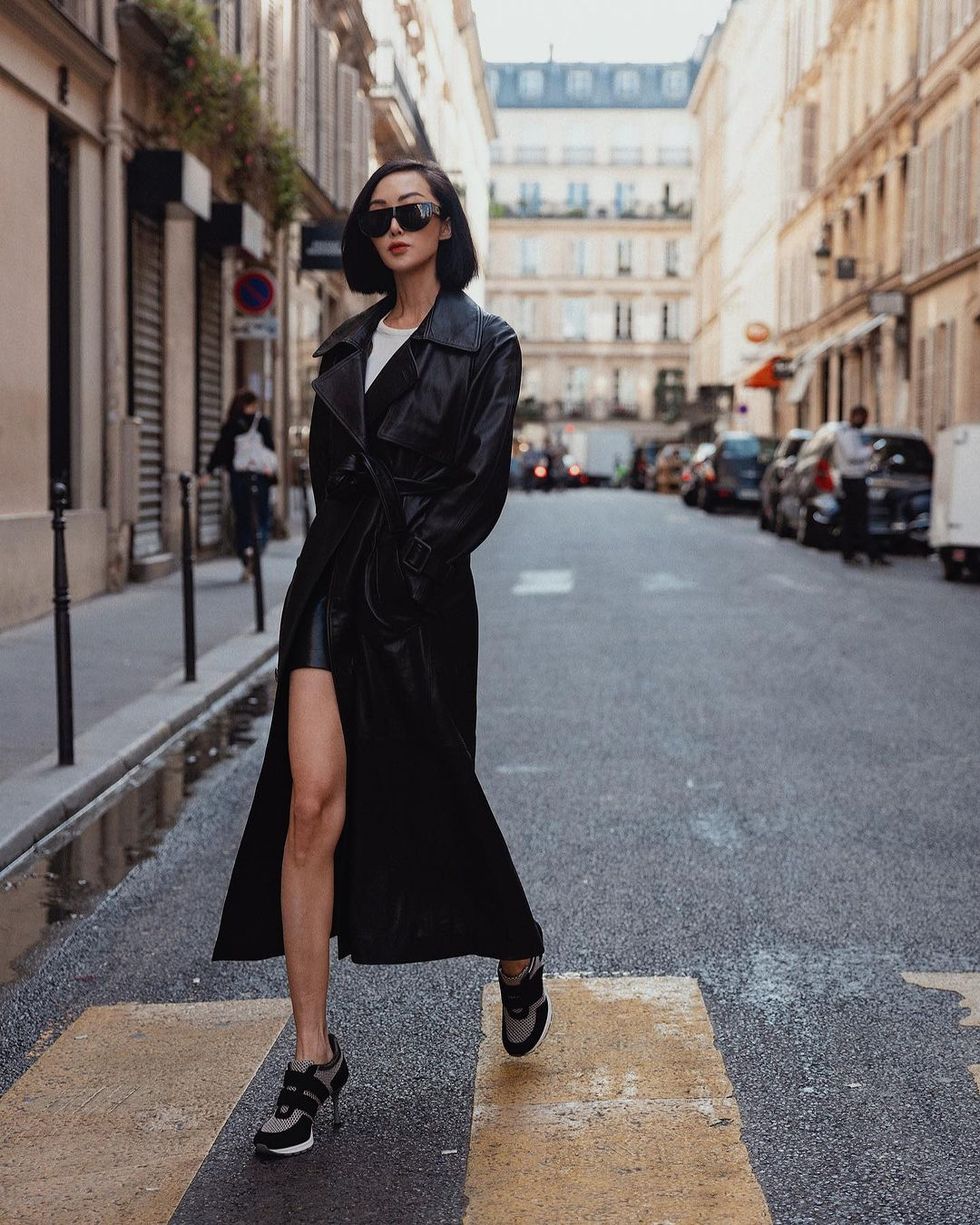 a person in a black coat and sunglasses walking down a street