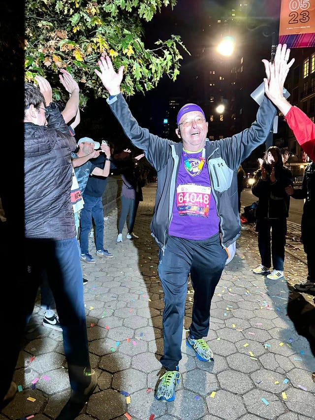 participant crossing the finish line at a nighttime event surrounded by cheering supporters