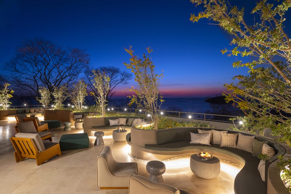 Outdoor lounge area with seating and fire pit overlooking the ocean at twilight.