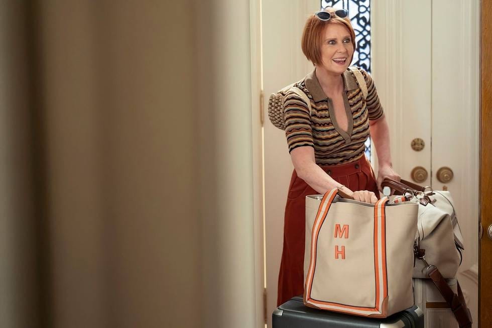 A person carrying luggage and a large tote bag in a doorway.