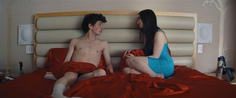 two individuals sitting on a bed engaged in conversation