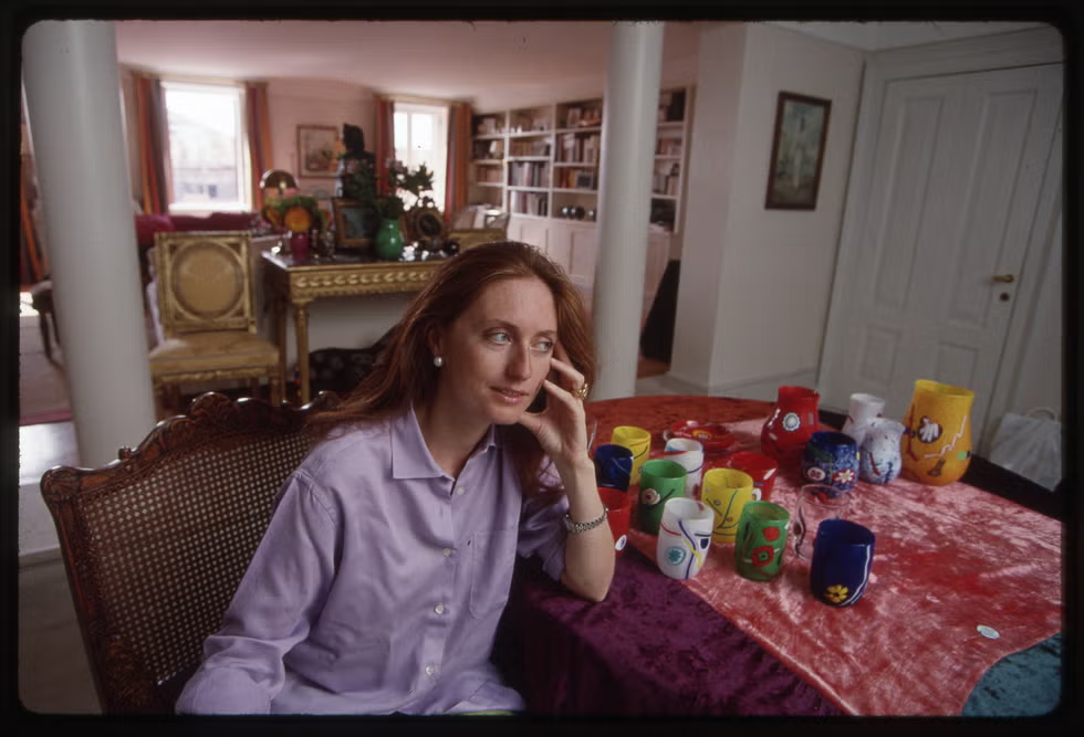 A woman seated at a table with colorful ceramic mugs in a well-furnished room.