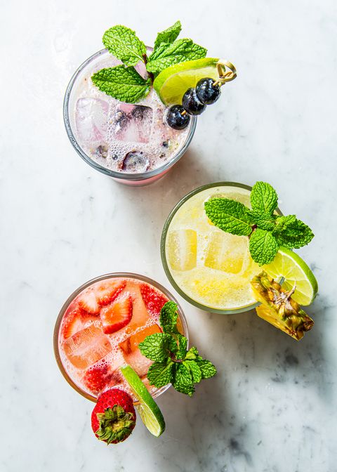 one strawberry, one pineapple, and one blueberry mojito, all garnished with mint and fruit on a white marble background