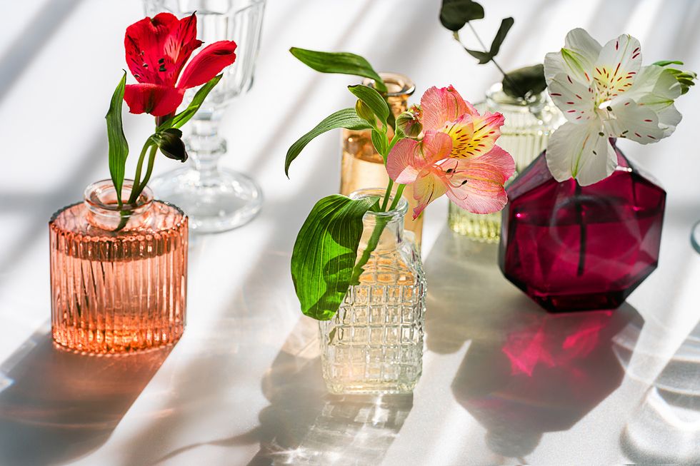summer scene with flowers in the colorful glass vases from perfume on pastel background with shadows sunlight and shadows minimal nature background copy space close up