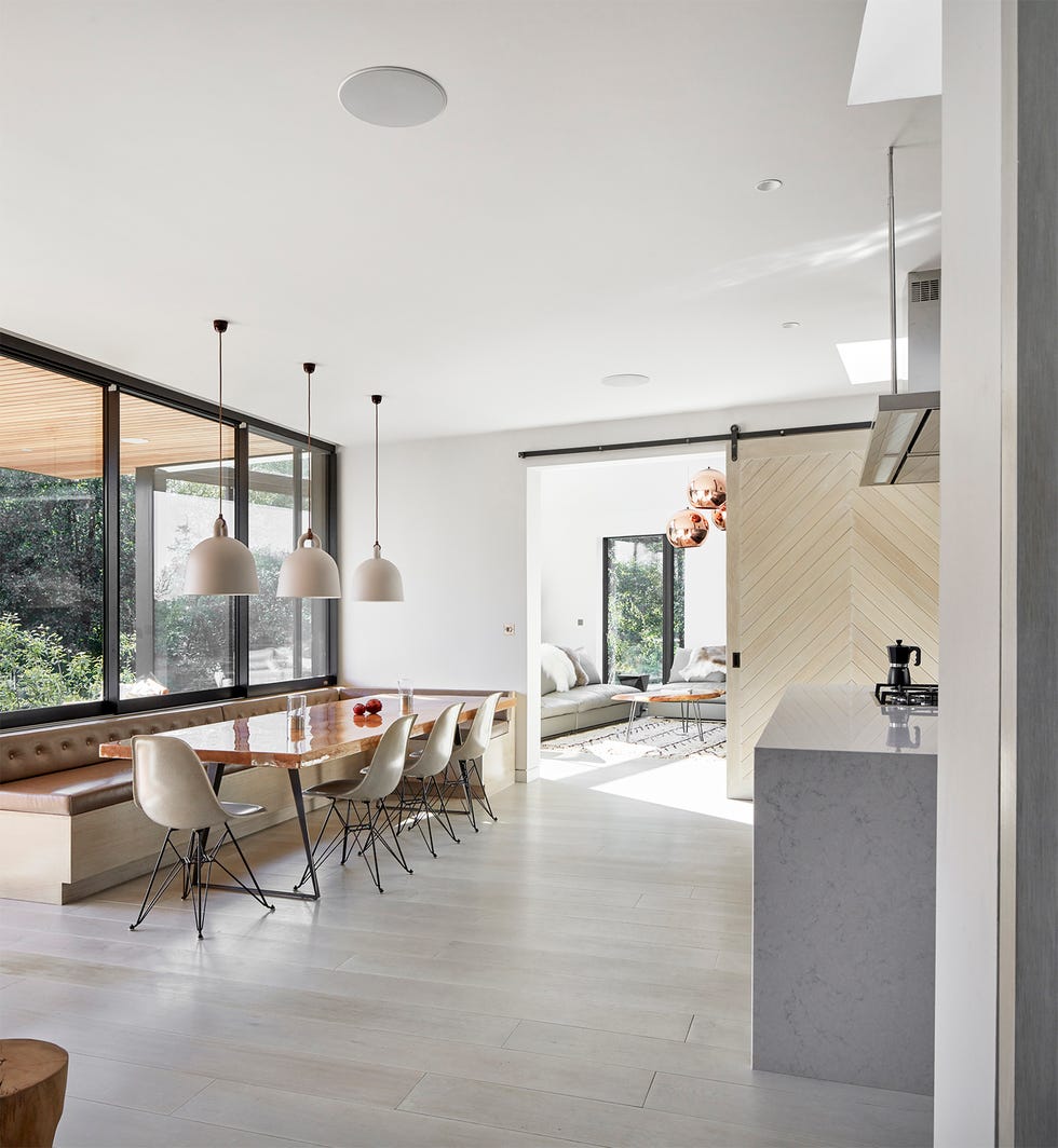 a view from the dining area through to the living room showing the long dining table, wooden floors, stone kitchen island and large windows