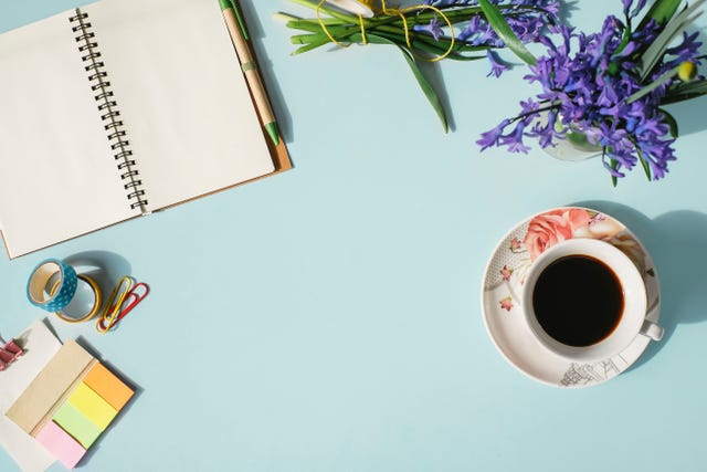 Notebook, office supplies, cup of coffee and spring flowers on light blue background