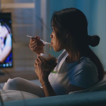 een vrouw eet noodles op de bank voor de tv