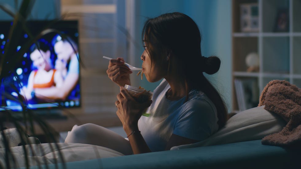 een vrouw eet noodles op de bank voor de tv