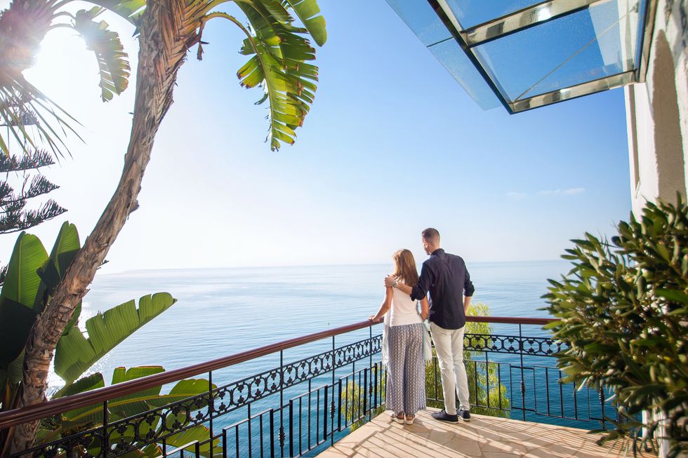 a man and woman kissing on a balcony overlooking the ocean