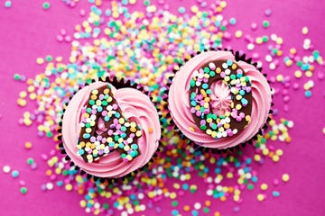 two chocolate cupcakes with pink frosting with a 4 and a 0 and sprinkles on top