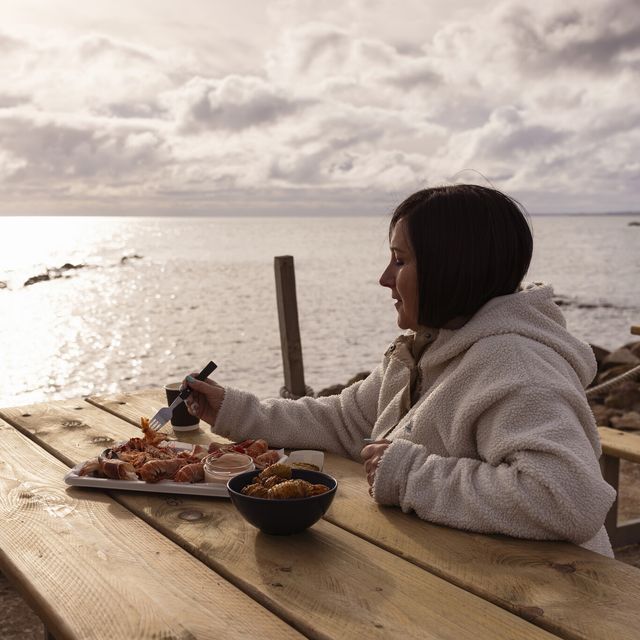 a person sitting at a table with food on it by the water