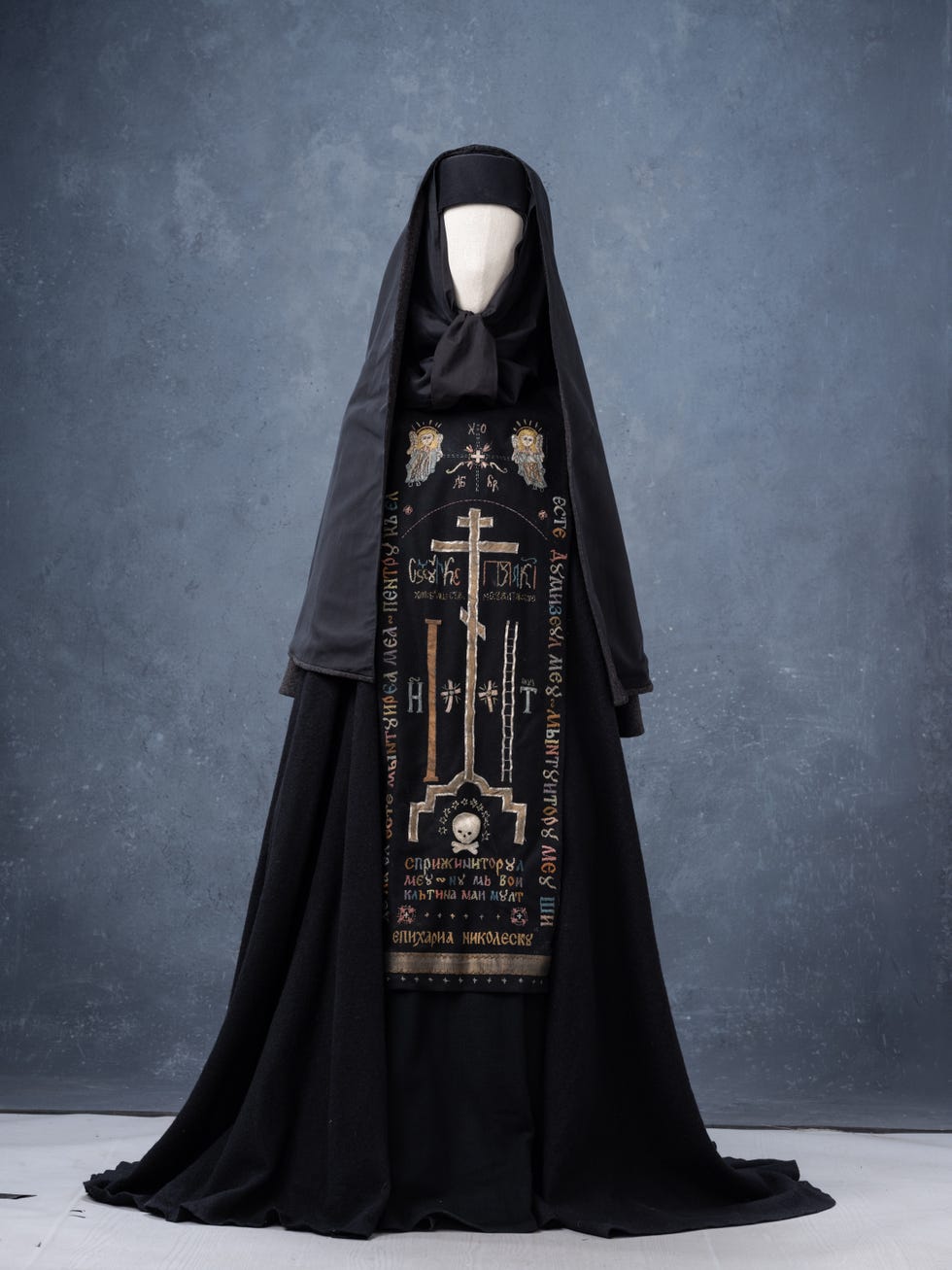 A black garment with religious embroidery displayed on a mannequin against a plain background