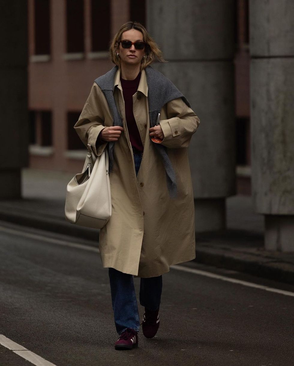 a person wearing a trench coat and sunglasses walking down a street