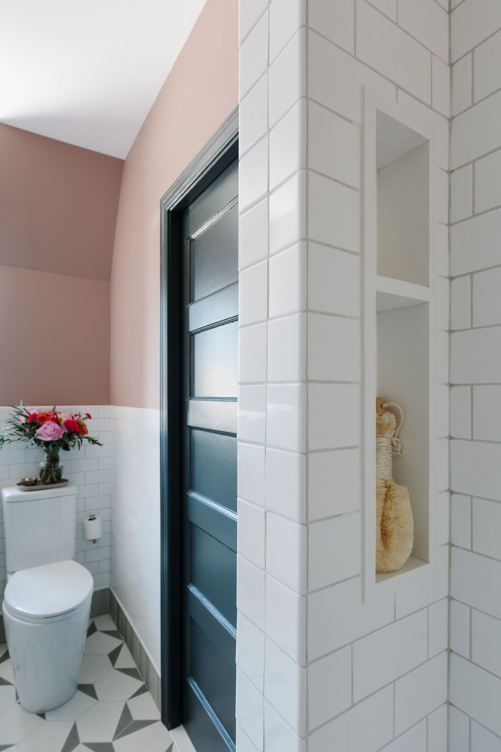 pink painted wall, white subway tile, white toilet, geometric white and gray tiles, built in shelving
