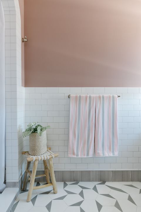 pink painted wall, white subway tile, wooden stool, white shower curtain, geometric white and gray tiles, pink and gray towels