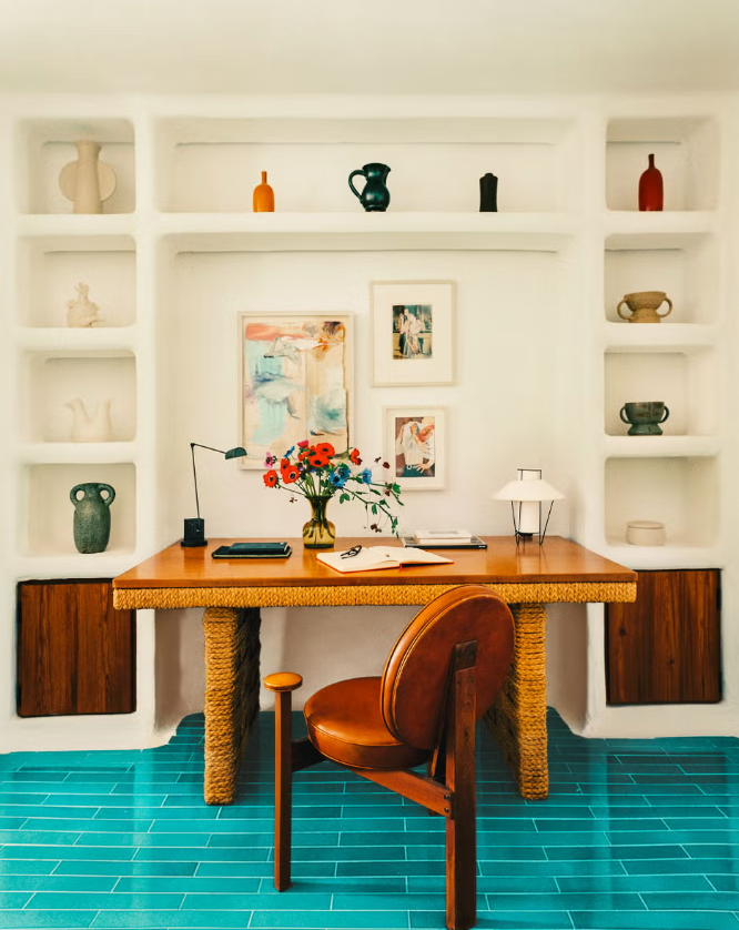 Home office featuring a wooden desk with a floral centerpiece and decorative items on shelves.