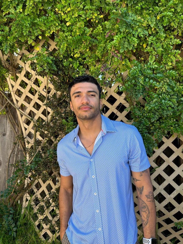 a man standing in front of a fence and a tree