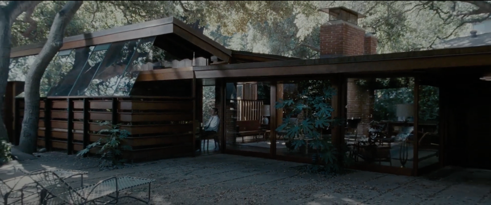 Modernist house surrounded by trees with a brick chimney and large windows.