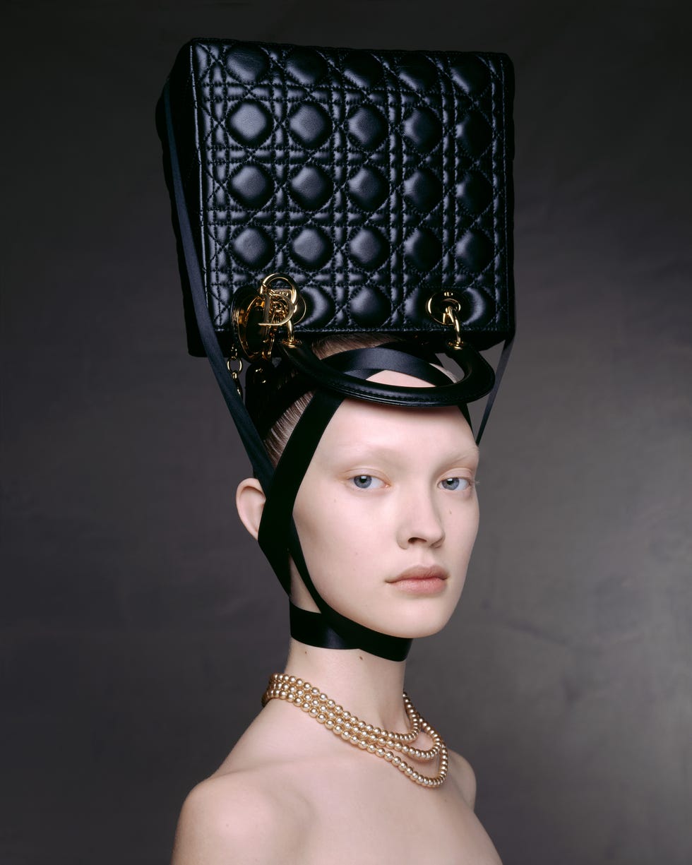 fashion model wearing a large black quilted handbag as a headpiece with a pearl necklace