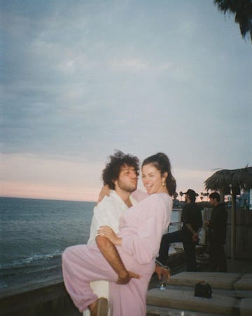 selena gomez and benny blanco embrace each other in front of a seaside sunset