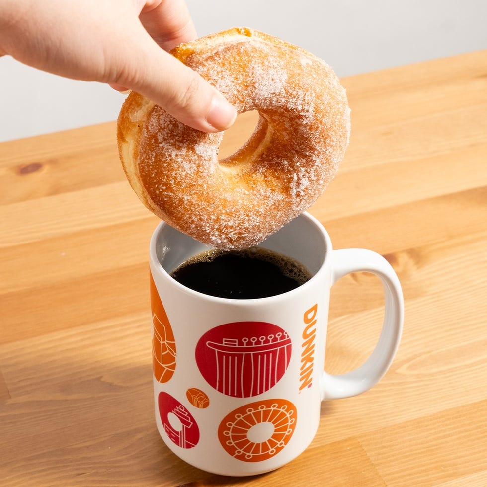a hand holding a donut above a coffee mug