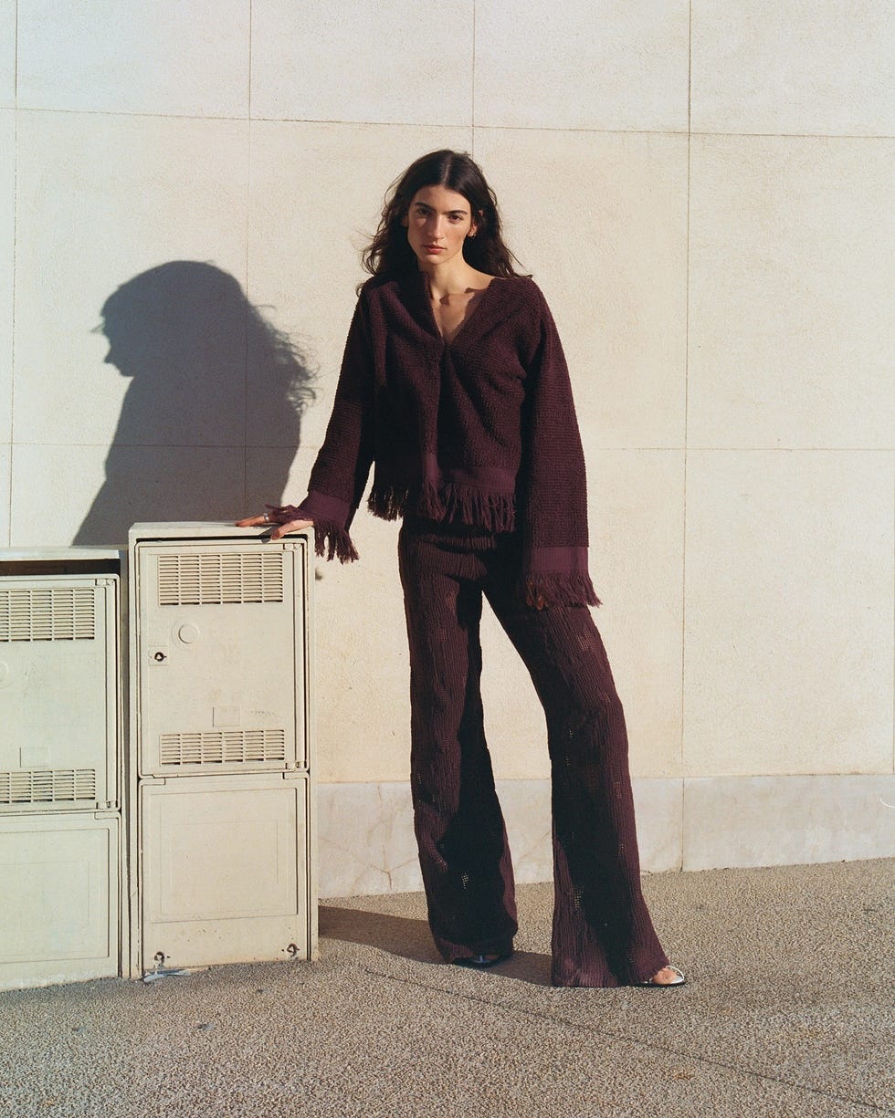 a person stands beside utility boxes against a textured wall