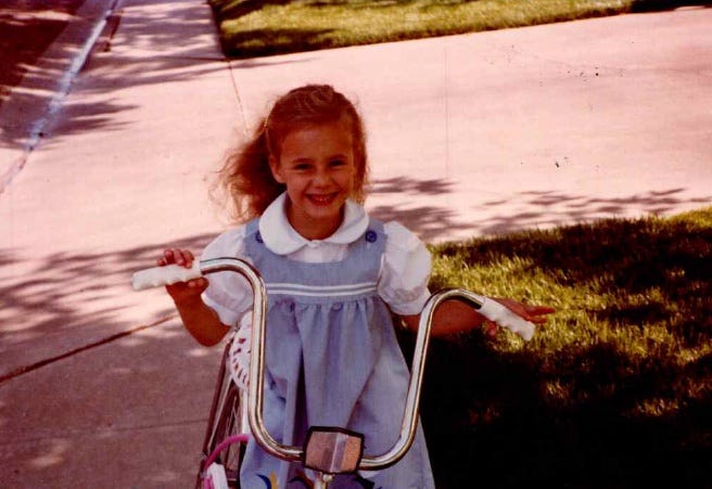 a child smiling while holding the handlebars of a bicycle