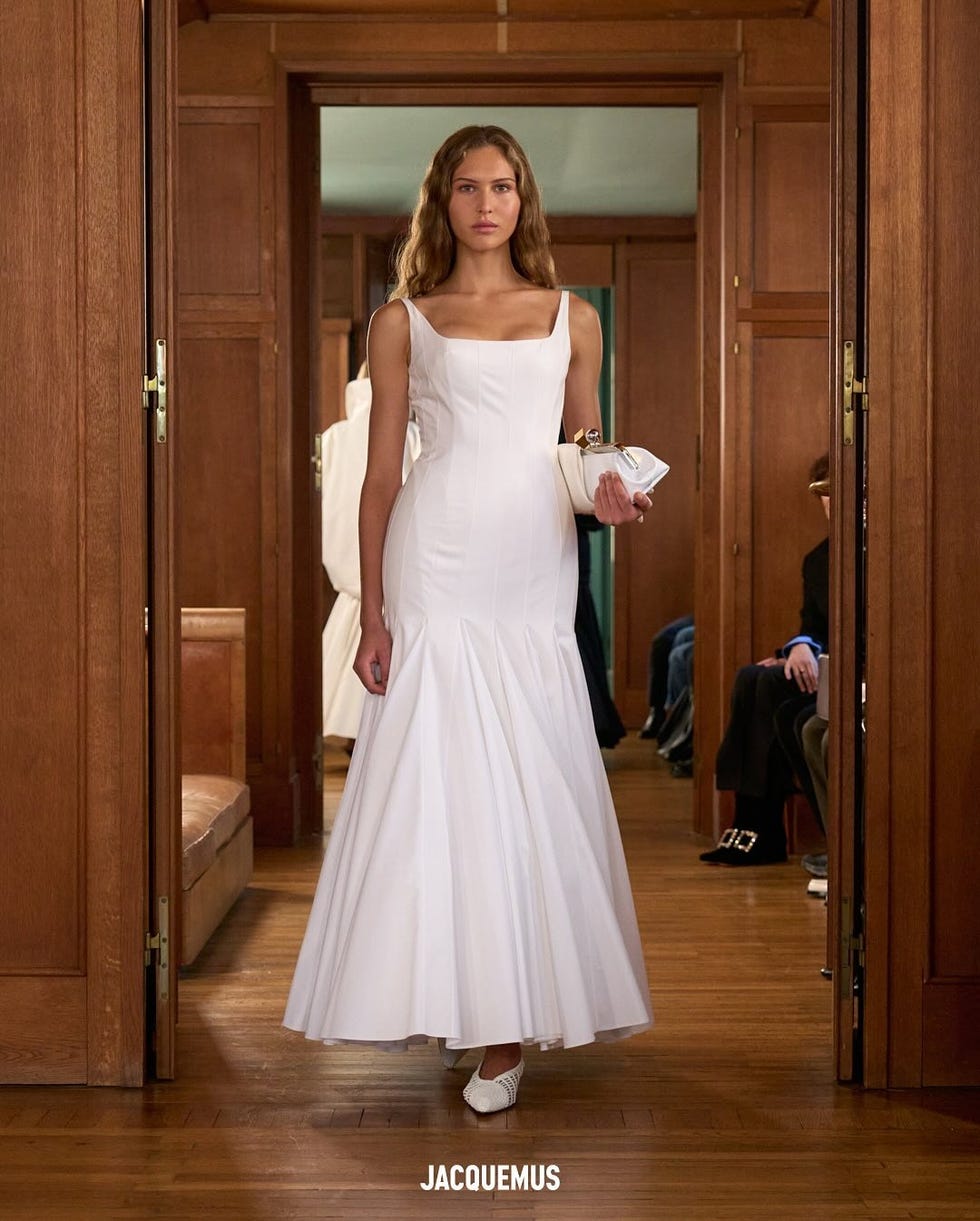 runway model showcasing a white dress in a wooden interior setting