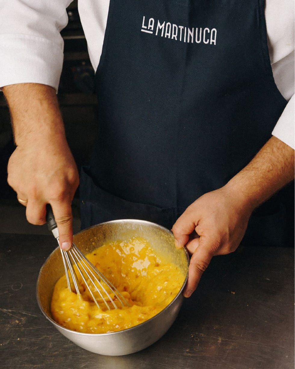 chef whisking a mixture in a bowl while wearing an apron